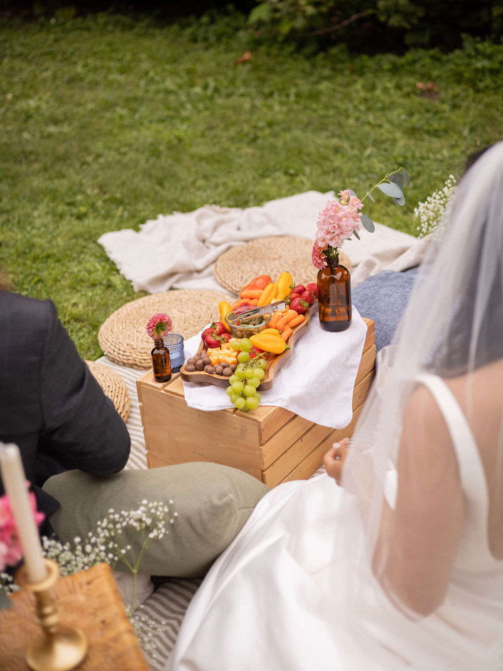 A wooden crate laid with a grazing board and bud vases, with blankets and cushions on the lawn at Cathedral Park