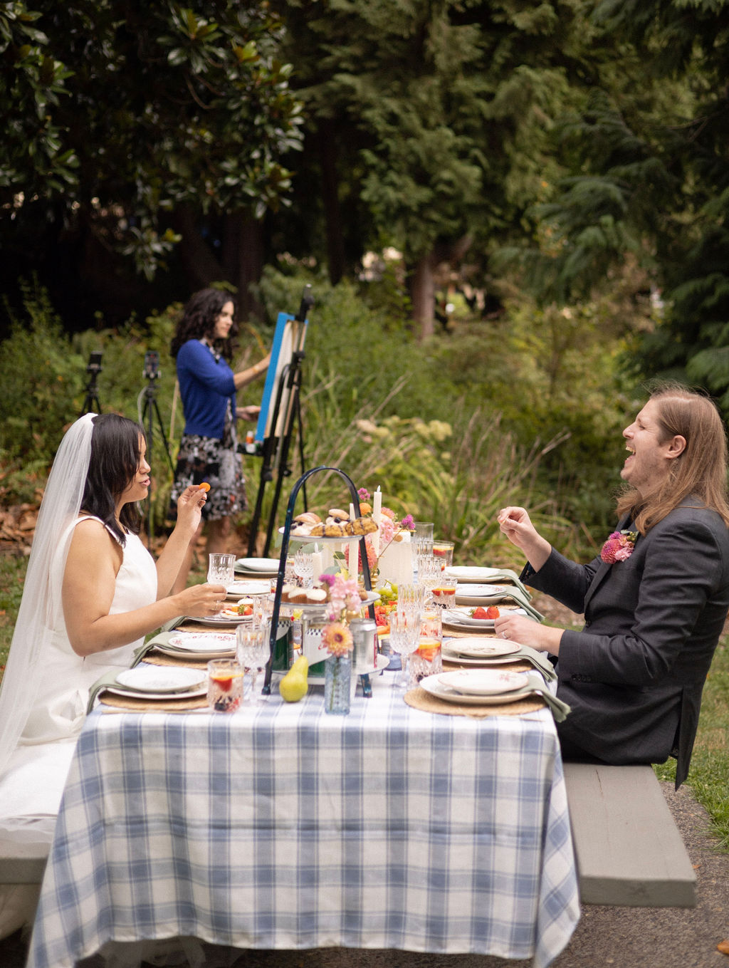Newlyweds at a laid picnic table at Cathedral Park with a live event painter working behind them