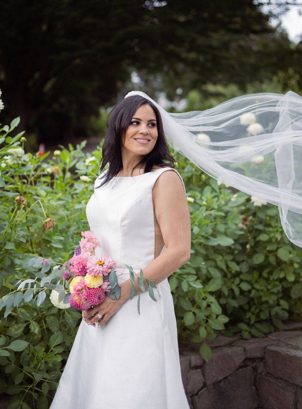 Bride holding a dahlia bouquet with her veil lifting in the wind at Cathedral Park