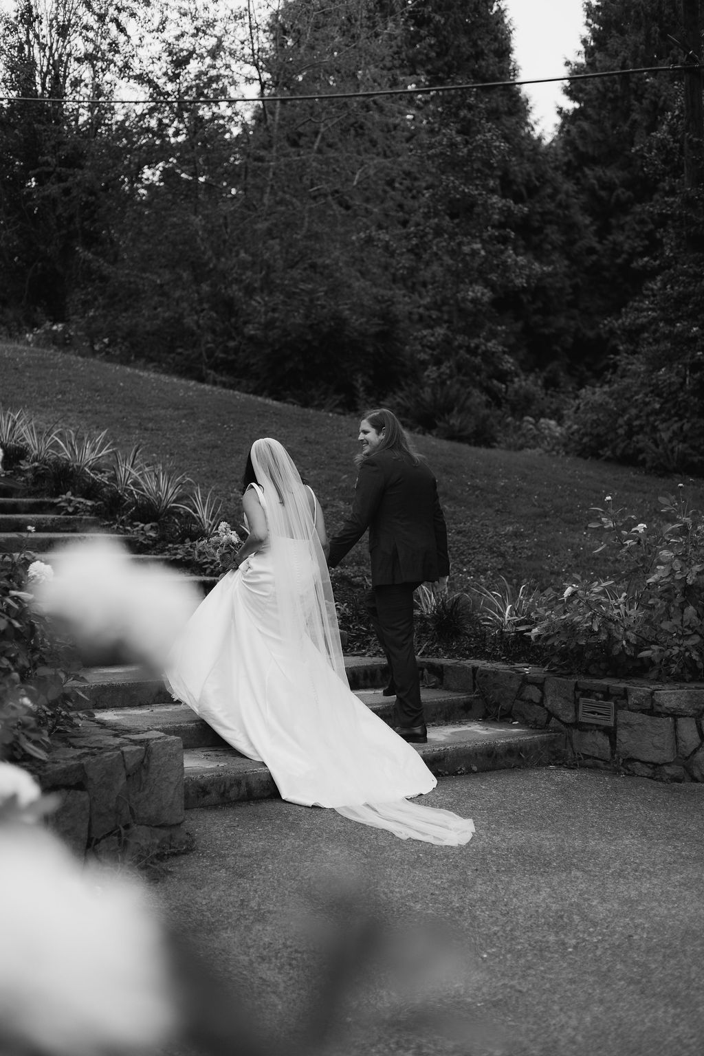 Black and white photograph of a bride and groom walking up the park steps